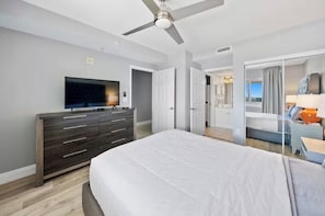 A hotel room with a large bed, a TV on a dresser, a ceiling fan, and a view of the outside. - Emerald Beach - A Gulf Front Resort Experience (Panama City Beach)
