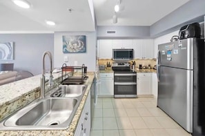 A modern kitchen with stainless steel appliances, white cabinetry, and a granite countertop. - Emerald Beach - A Gulf Front Resort Experience (Panama City Beach)