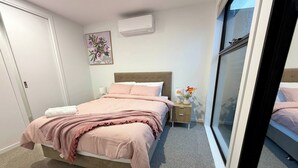 Une chambre à coucher comprenant un lit, une table de chevet, un climatiseur fixé au mur et une fenêtre.