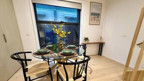 Un coin repas avec une table en verre entourée de chaises, un vase avec des fleurs jaunes et une vue sur un bâtiment à l’extérieur.