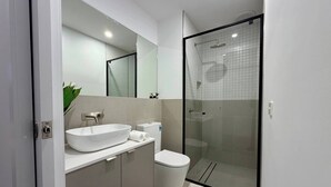 Une salle de bain moderne avec un lavabo blanc, des toilettes et une douche à parois de verre.