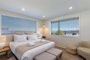 A hotel room with a large bed, two bedside tables, a bench, and a view of the cityscape through the windows. - Views on Beachman - pet friendly with lake views (Taupo)