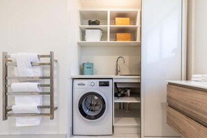 A compact laundry area with a washing machine, a drying rack, and storage shelves. - Views on Beachman - pet friendly with lake views (Taupo)