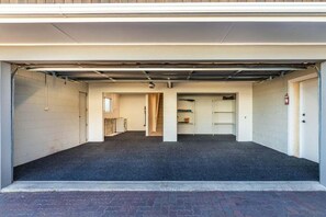 A covered parking garage with a flat floor, a fire extinguisher mounted on the wall, and a door leading to a stairwell. - Views on Beachman - pet friendly with lake views (Taupo)