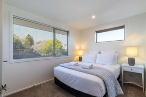 A bedroom with a large bed, two bedside lamps, a window with blinds, and a small skylight. - Views on Beachman - pet friendly with lake views (Taupo)