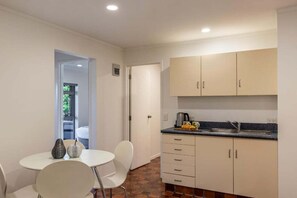 A compact kitchen with white cabinets, a sink, and a dining area with a table and chairs. - Views on Beachman - pet friendly with lake views (Taupo)