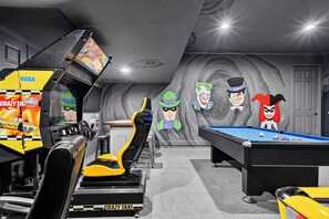 A gaming room with a pool table, racing simulator, and arcade machines. - 7BR Solara Resort Home with Private Pool & Games (Kissimmee)