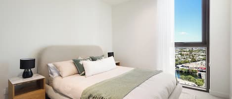 A modern bedroom with a bed, nightstand, and a view of a cityscape through a large window.