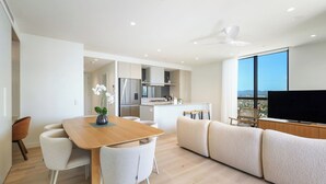 A modern living space with a dining area, kitchen, and a large window offering a view. - Luxe Escape at Yves at Mermaid Beach (Mermaid Beach)