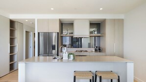 A modern kitchen with a central island, stainless steel appliances, and a minimalist design. - Luxe Escape at Yves at Mermaid Beach (Mermaid Beach)