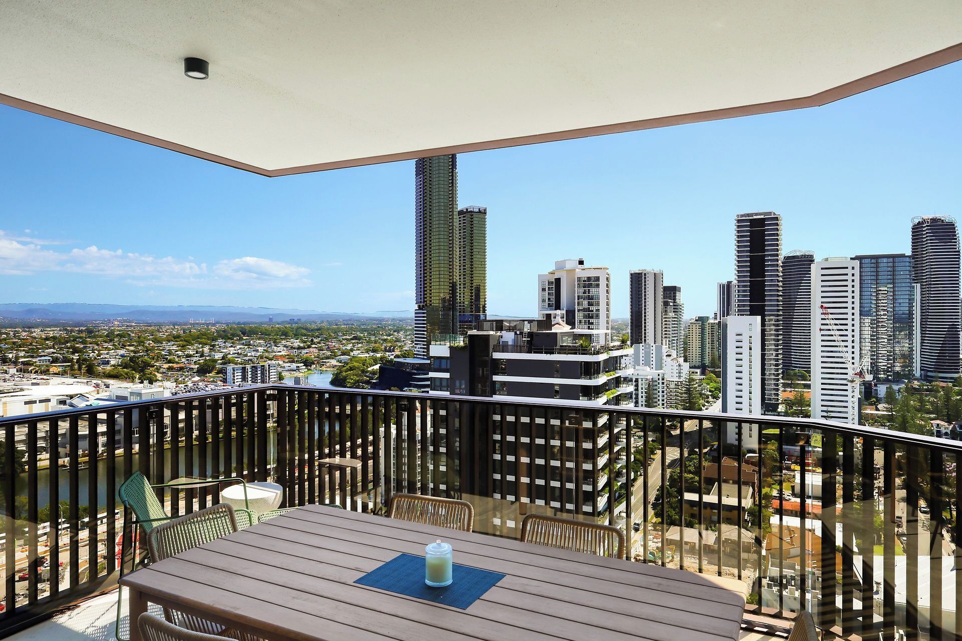 A balcony with a view of a cityscape, including high-rise buildings and a distant mountain range.