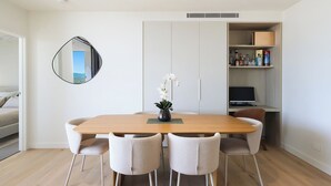 A modern dining area with a wooden table, four chairs, a vase with white flowers, and a built-in shelf with various items. - Luxe Escape at Yves at Mermaid Beach (Mermaid Beach)