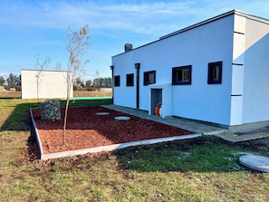 A modern building with a flat roof, a small entryway, and a landscaped garden with a tree and a stone structure.