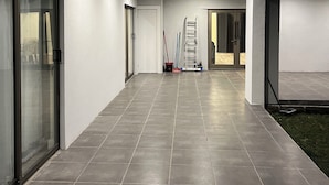 A hallway with a tiled floor, glass doors, and a ladder leaning against a wall.