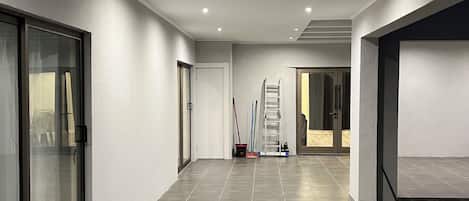 A hallway with a tiled floor, glass doors, and a ladder leaning against a wall.