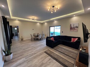 Una sala moderna con un sofá modular, una mesa de comedor y sillas. Hay un ventanal con vistas al exterior.