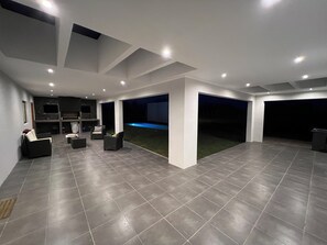 A spacious indoor area with a tiled floor, a flat-screen TV mounted on the wall, and a seating area with sofas and chairs.