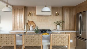 Eine moderne Küche mit Holzausstattung, einem Edelstahlkühlschrank, einem Einbauherd und Pendelleuchten.