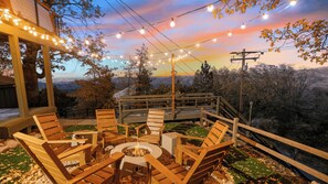 An outdoor seating area with wooden furniture and a fire pit, overlooking a scenic landscape. - The A-list by Avantstay A-frame Cabin w/ Hot Tub + Firepit & EV Charger Near Trails + Lake (Lake Arrowhead)