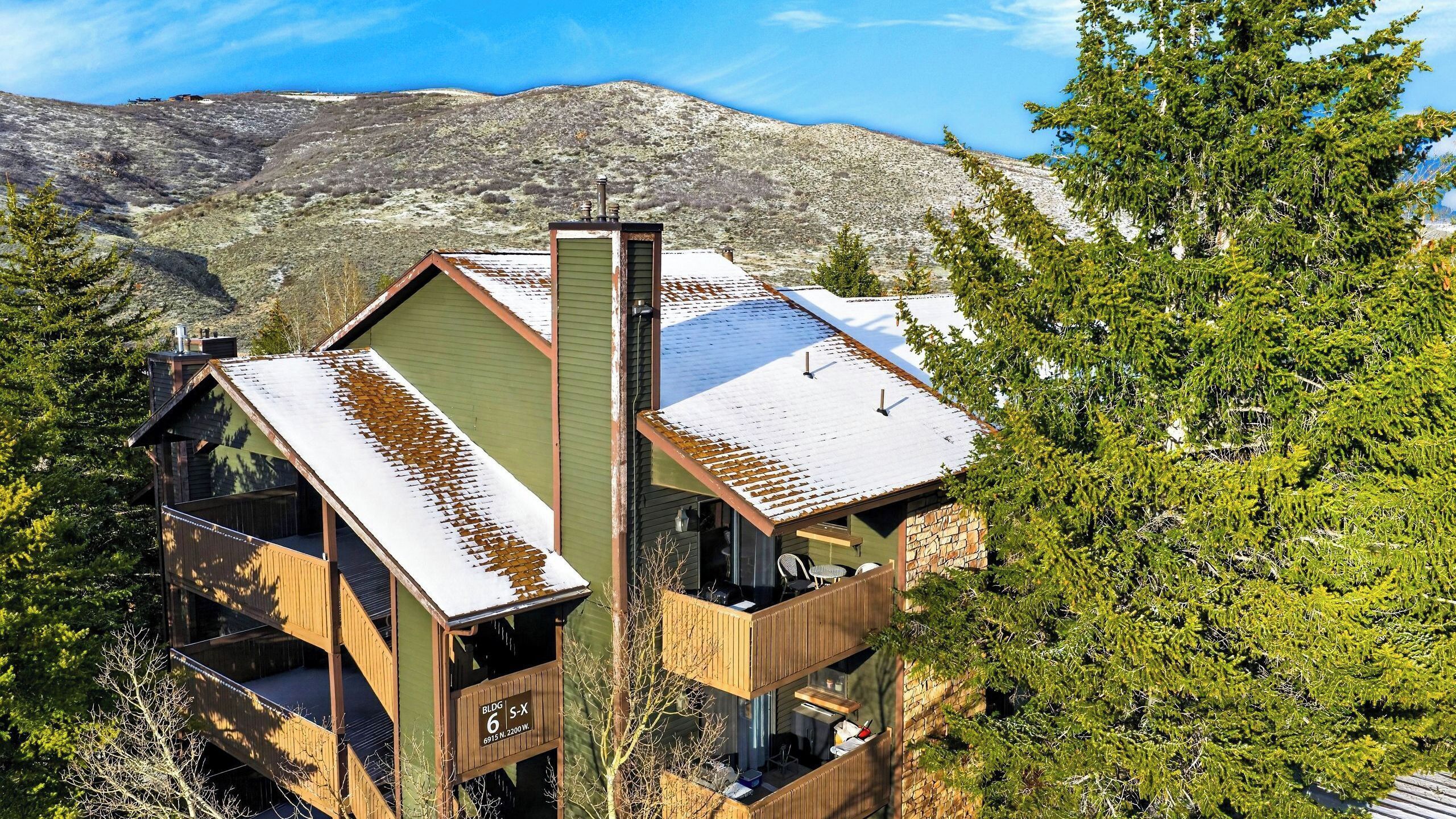 A multi-level wooden cabin with a balcony, set against a mountainous backdrop.