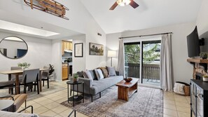 A modern living room with a grey sofa, coffee table, and dining area with chairs. There is a kitchen visible in the background, a large window with curtains, and a ceiling fan. - Powder Perch by Avantstay Hot Tub + Pool + Mountain-view Balcony Mins to the Slopes + Trails (Park City)