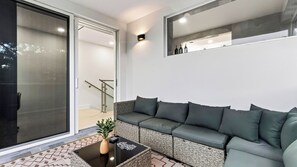 A modern living room with a grey sofa, a coffee table with a plant, and a sliding glass door leading to a staircase. - Palm Perch by Avantstay Shared Pool Deck + BBQ + Skyline Balcony Walk to Las Olas (Fort Lauderdale)