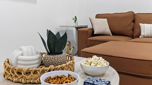 A living room with a brown sofa, a white bowl of popcorn, a white bowl of pretzels, a white decorative object, and a potted plant. - Palm Perch by Avantstay Shared Pool Deck + BBQ + Skyline Balcony Walk to Las Olas (Fort Lauderdale)