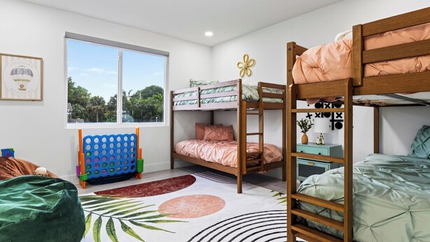 A bunk bed room with a window, a blue headboard, a small table, and a green couch. - Palm Perch by Avantstay Shared Pool Deck + BBQ + Skyline Balcony Walk to Las Olas (Fort Lauderdale)