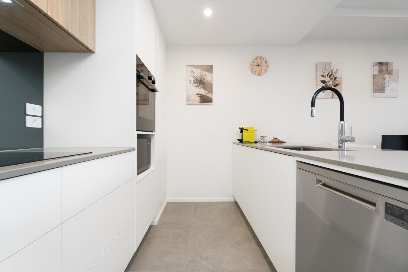 A modern kitchen with white cabinetry, stainless steel appliances, a black faucet, and a clock on the wall.