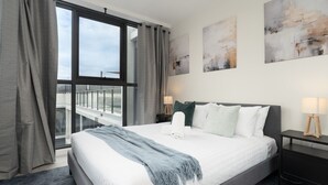 A hotel room with a large bed, a view of the city through a window, and artwork on the walls. - Inner North 1BR Near Braddon & Dickson (Lyneham)