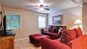 A living room with a ceiling fan, a red sofa, a wooden cabinet, and a window with blinds. - Downtown Diggs by Avantstay Spa + Chef's Kitchen Walk to Wineries (Paso Robles)