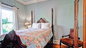 Ein Schlafzimmer mit einem Himmelbett, einem Nachttisch mit Lampe und einem Sessel.