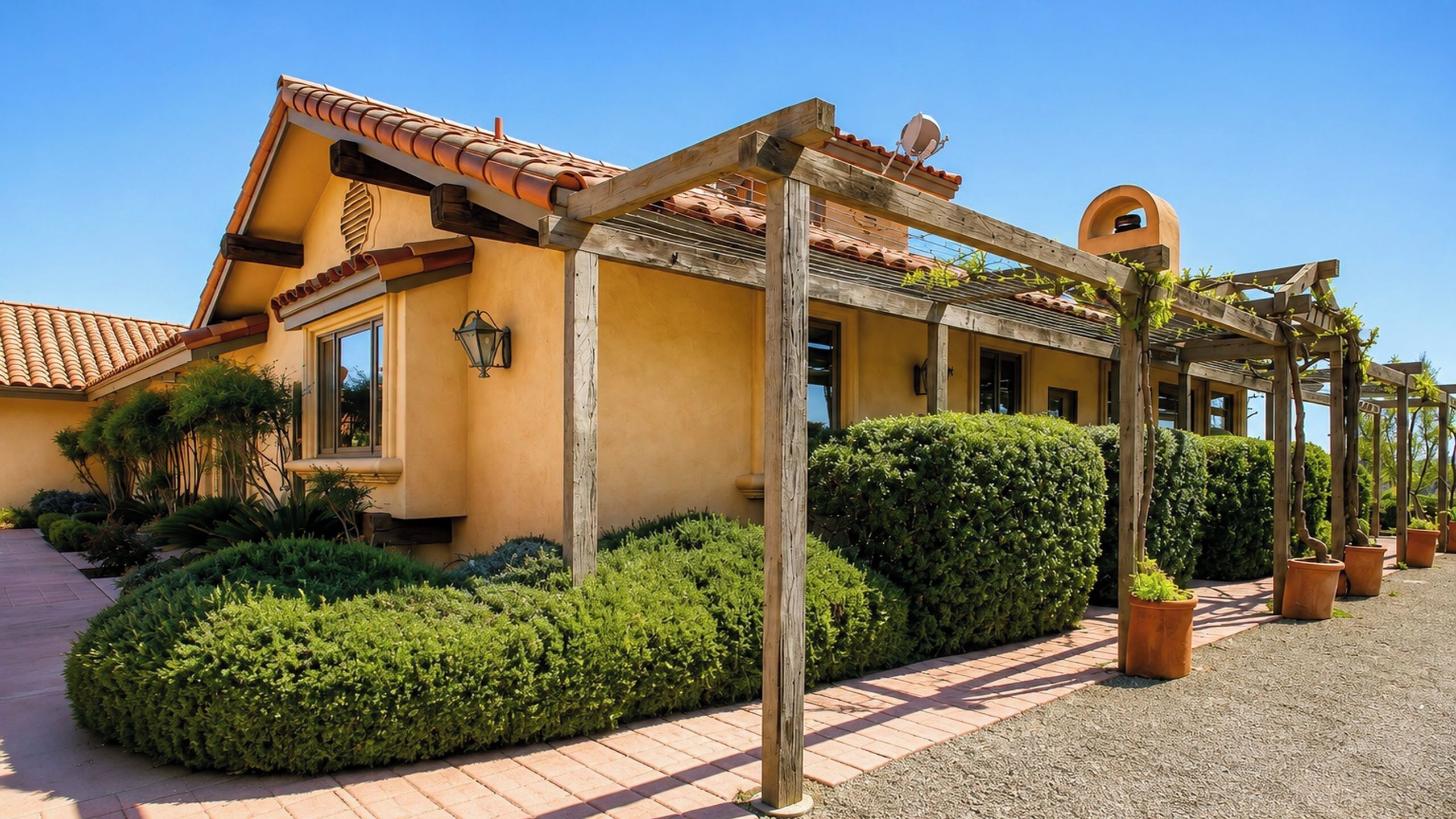 A building with a tiled roof, wooden pergola, and well-maintained hedges.