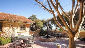 Eine Terrasse mit Gartenmöbeln, einer Fontäne und einem Baum.