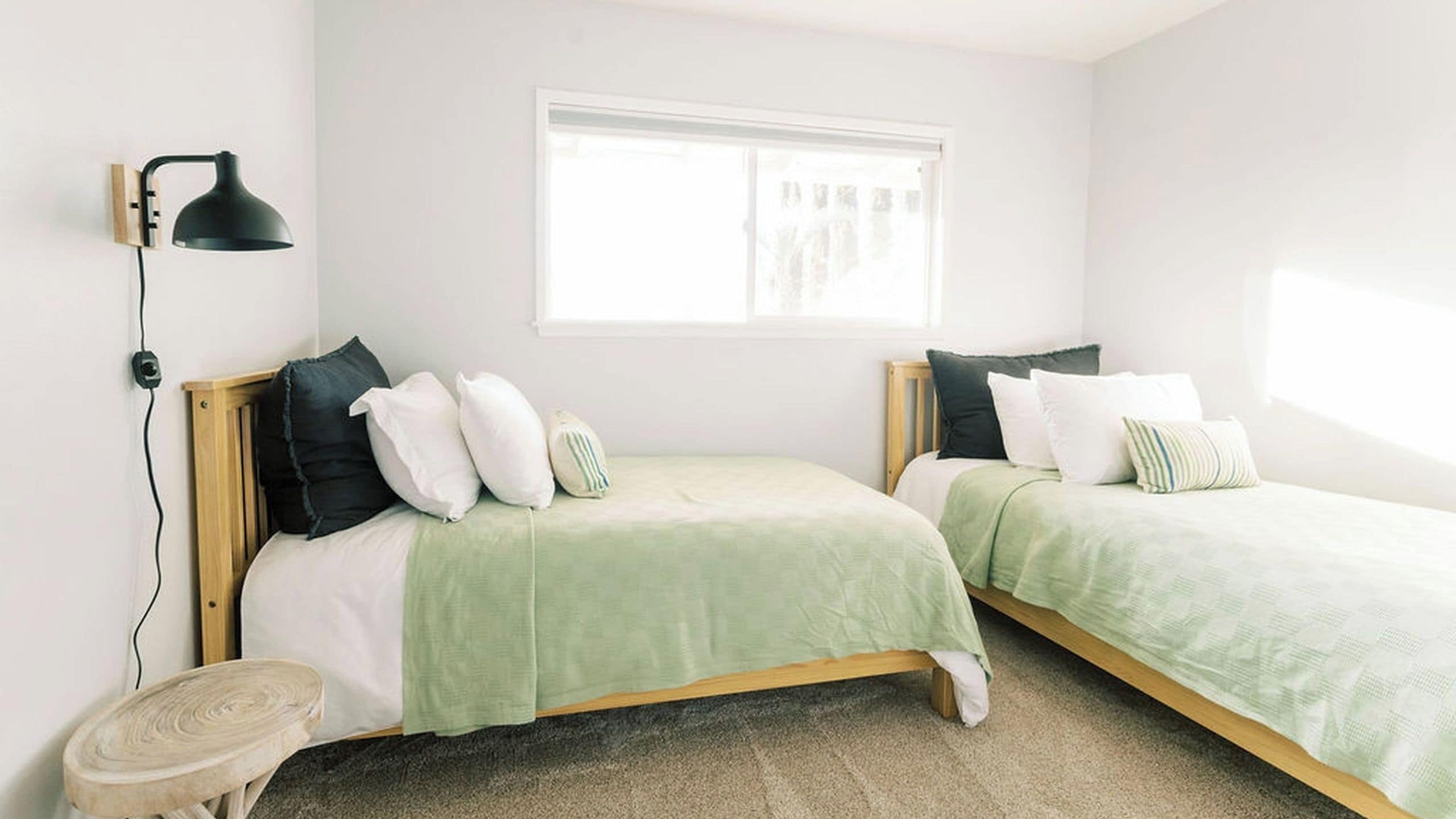 A bedroom with two beds, a window, a lamp, and a small table.