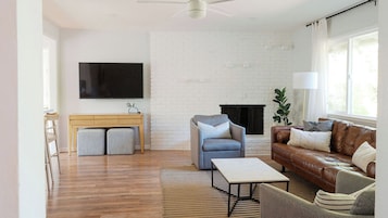 Una sala de estar con pared de ladrillo blanco, un televisor de pantalla plana, un sofá de cuero marrón y un banco de madera.