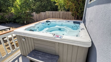A hot tub with a control panel, a wooden deck, and a wooden fence in the background.