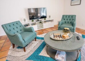 A living room with two teal armchairs, a round coffee table, and a flat-screen TV on a white cabinet. -  New Property! The Hidden Catch.. 2-bdr house on the water and great for fishing (Lauderdale-by-the-Sea)