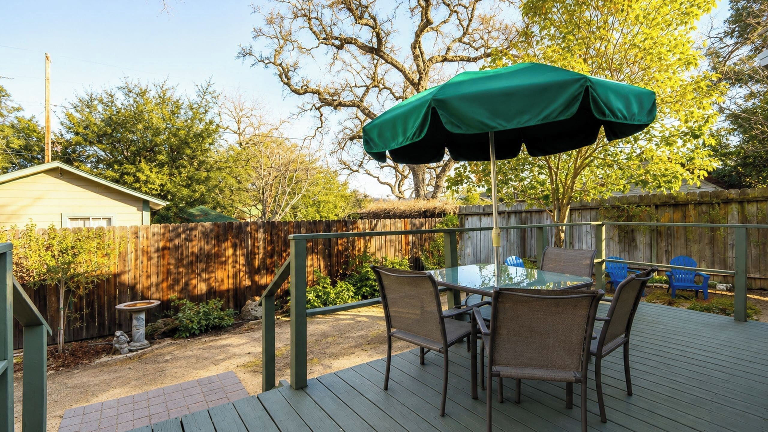 Un patio con una mesa y sillas, una sombrilla verde y una terraza de madera.