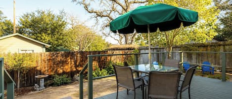 Un patio con una mesa y sillas, una sombrilla verde y una terraza de madera.