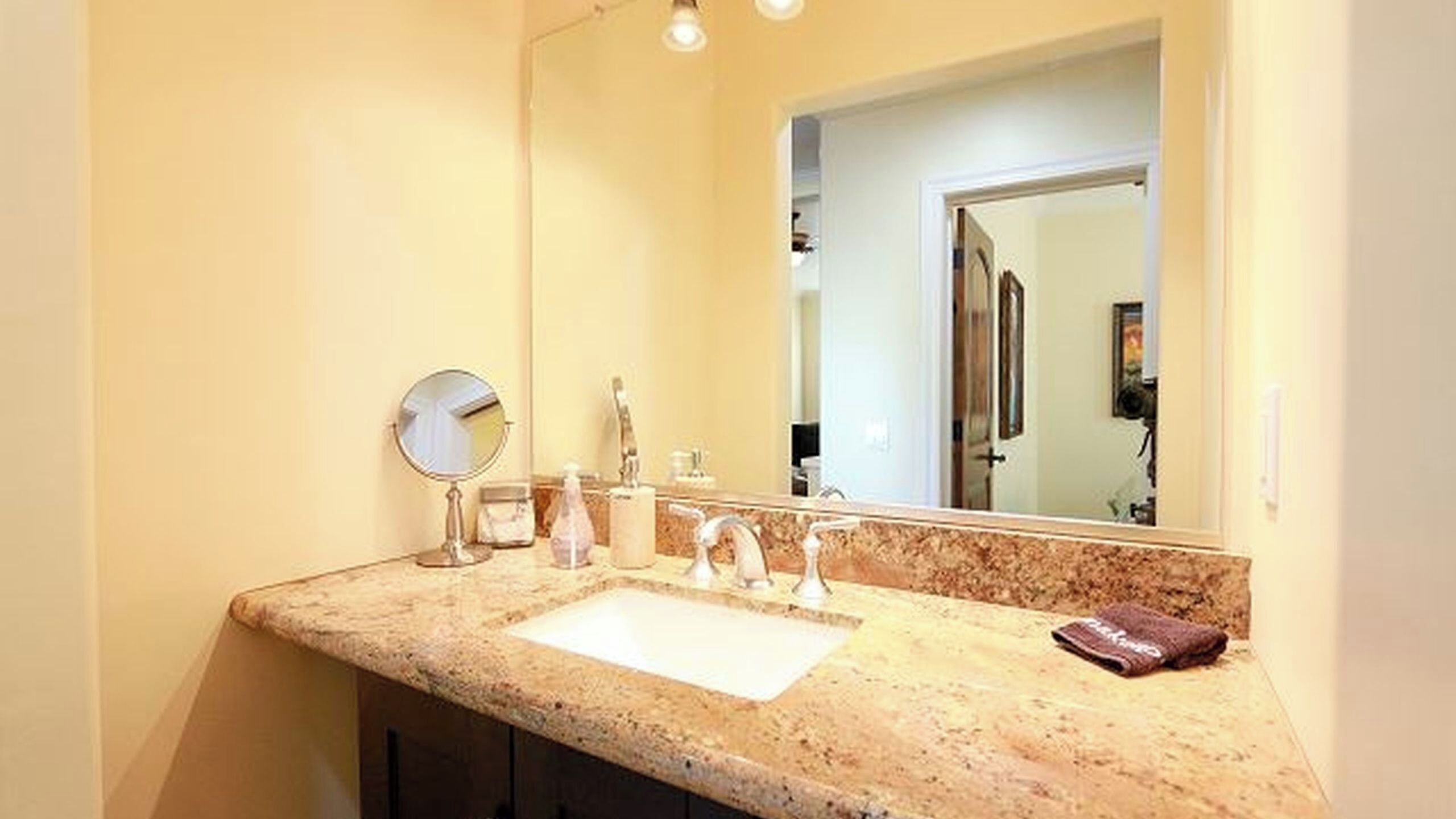 A bathroom with a granite countertop, a sink, a mirror, and a towel.