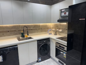 Eine moderne Küche mit weißen Schränken, einem schwarzen Geschirrspüler, einer Waschmaschine und einem schwarzen Kühlschrank.