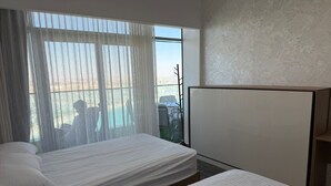 Ein Hotelzimmer mit zwei Betten, einem großen Fenster mit leichtem Vorhang und Blick ins Freie.