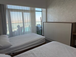 Ein Hotelzimmer mit zwei Betten, einem großen Fenster mit leichtem Vorhang und Blick ins Freie.