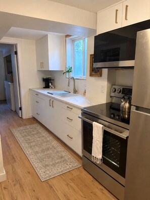 A modern kitchen with white cabinetry, a stainless steel refrigerator, an oven, and a coffee maker. - Bright 2BR Basement Apt - Near BSU & Micron (Boise)