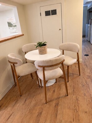 A dining area with a round table and four chairs, a potted plant on the table, and a door with a vent. - Bright 2BR Basement Apt - Near BSU & Micron (Boise)