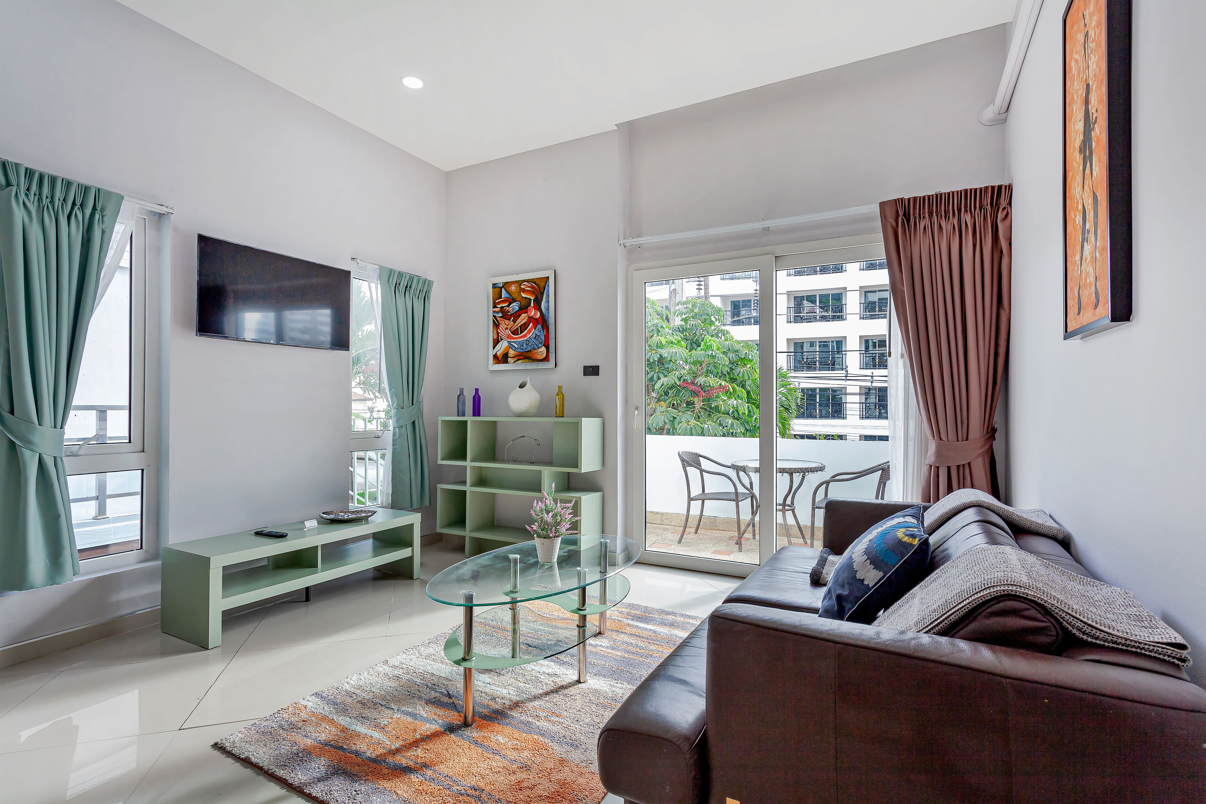 Un salon moderne avec une table basse en verre, un canapé, un téléviseur et un balcon offrant une vue sur les immeubles.