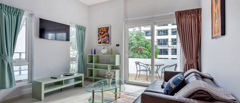 Un salon moderne avec une table basse en verre, un canapé, un téléviseur et un balcon offrant une vue sur les immeubles.