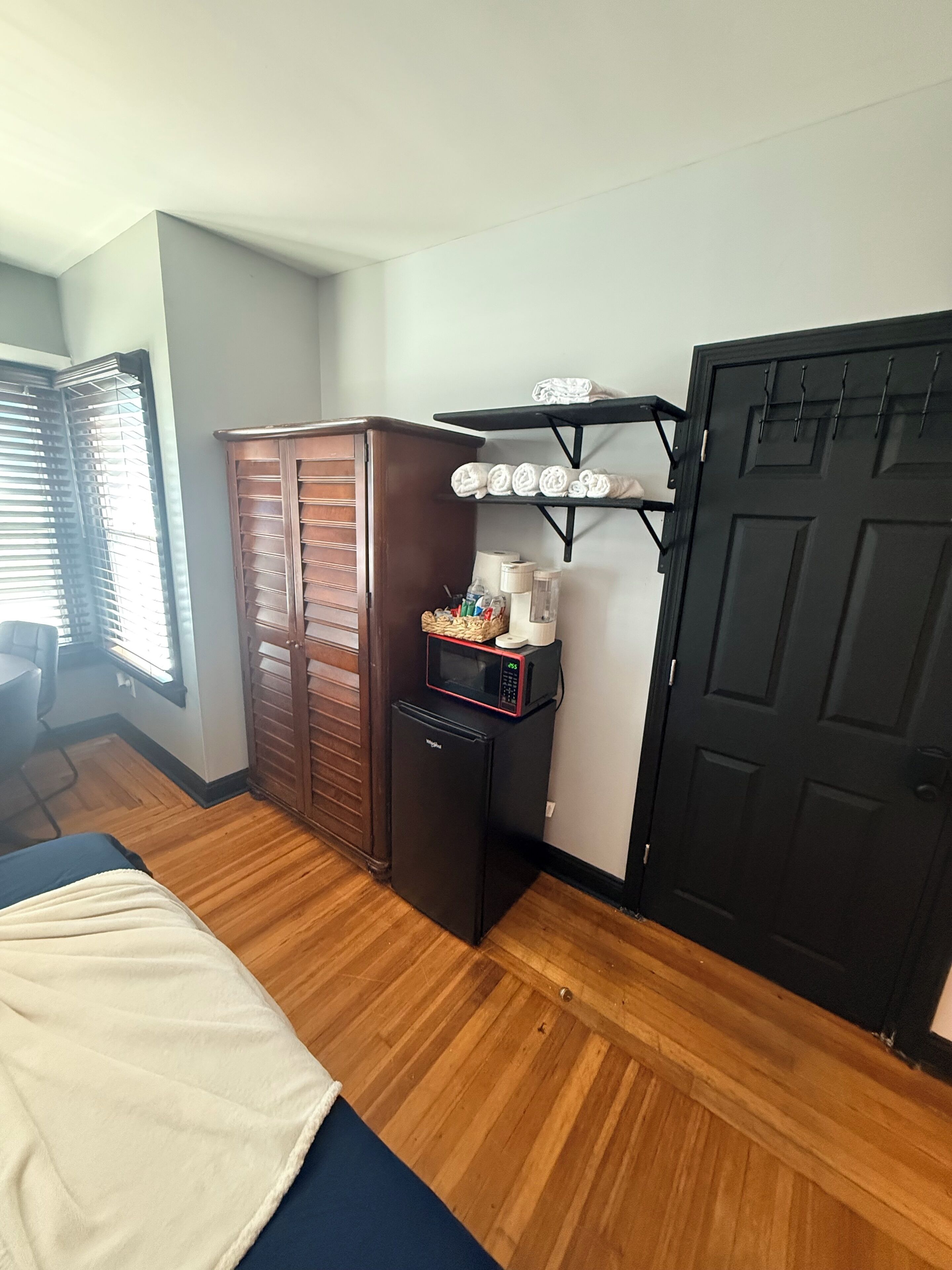 A room with a bed, a wardrobe, a microwave, and a door with hooks.