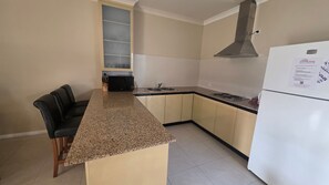 A kitchen with a granite countertop, a black chair, a built-in oven, and a white refrigerator.